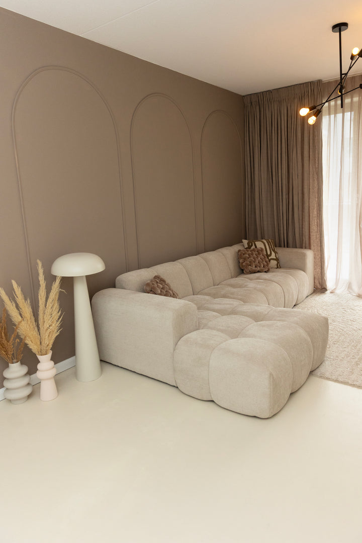 Sfeervolle woonkamer met beige wanden gedecoreerd met Velida flexlijsten in boogvormen achter een lichte modulaire bank
