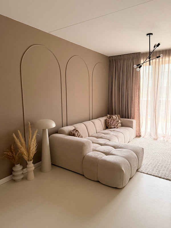 Japandi interieurstijl met taupe muren en wandpanelen gemaakt van flexibele sierlijsten, gecombineerd met een beige bank en zwarte hanglamp.