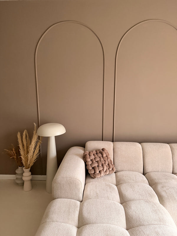 Minimalistische wanddecoratie met booglijsten, gestyled met een witte paddenstoellamp, droogbloemen in vazen en een knoopkussen