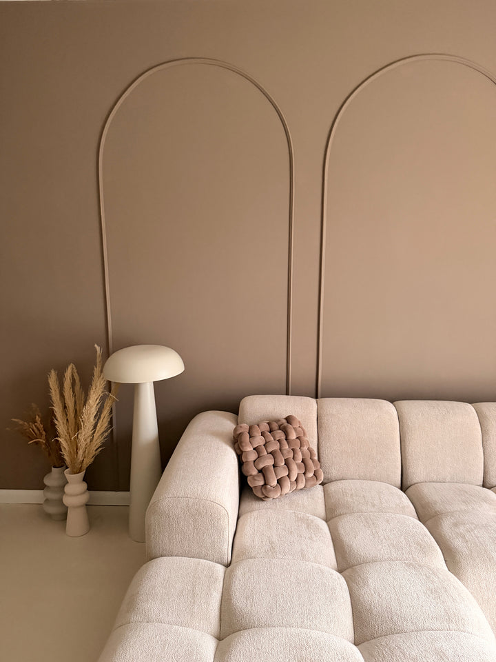 Minimalistische wanddecoratie met booglijsten, gestyled met een witte paddenstoellamp, droogbloemen in vazen en een knoopkussen