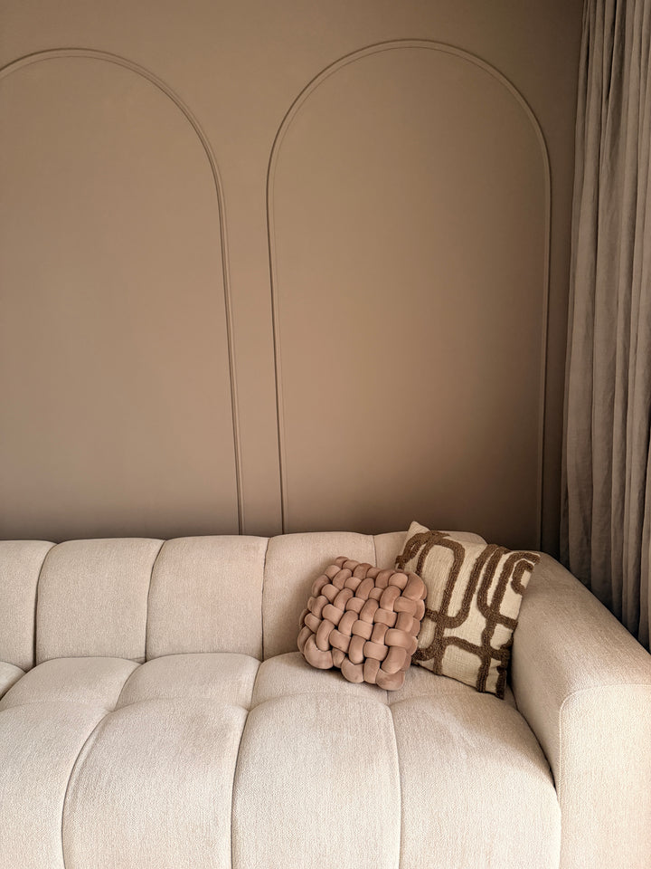 Detail van beige muurverf en flexibele wandlijsten in een boog, gecombineerd met textuurrijke kussens op de bank